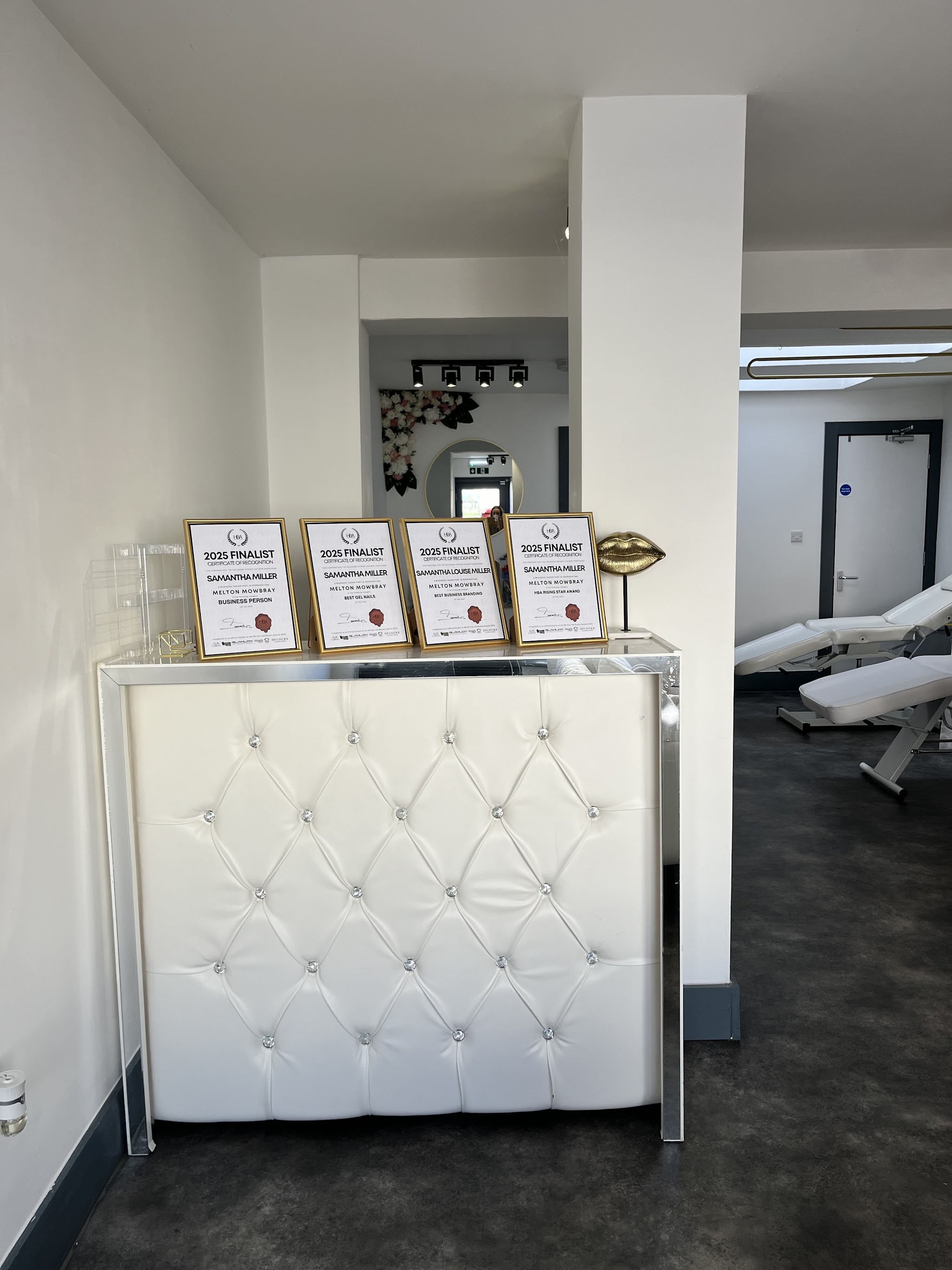 Our white tufted reception desk with the four 2025 finalist certificates